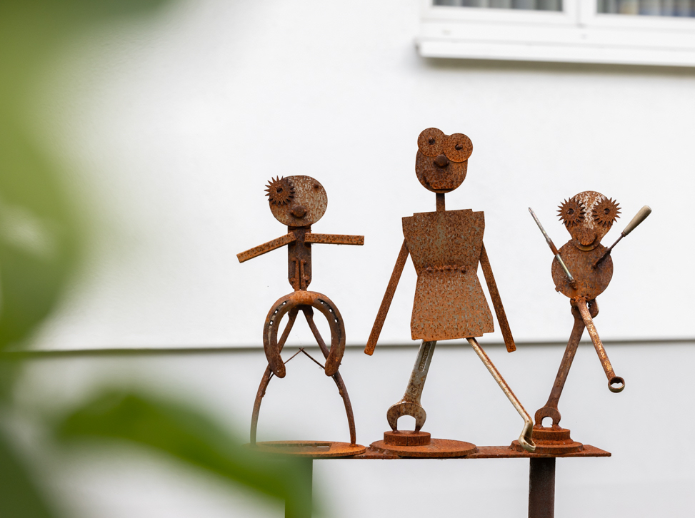 Drei Figuren aus Stahl in Rostoptik, vor einer Hauswand